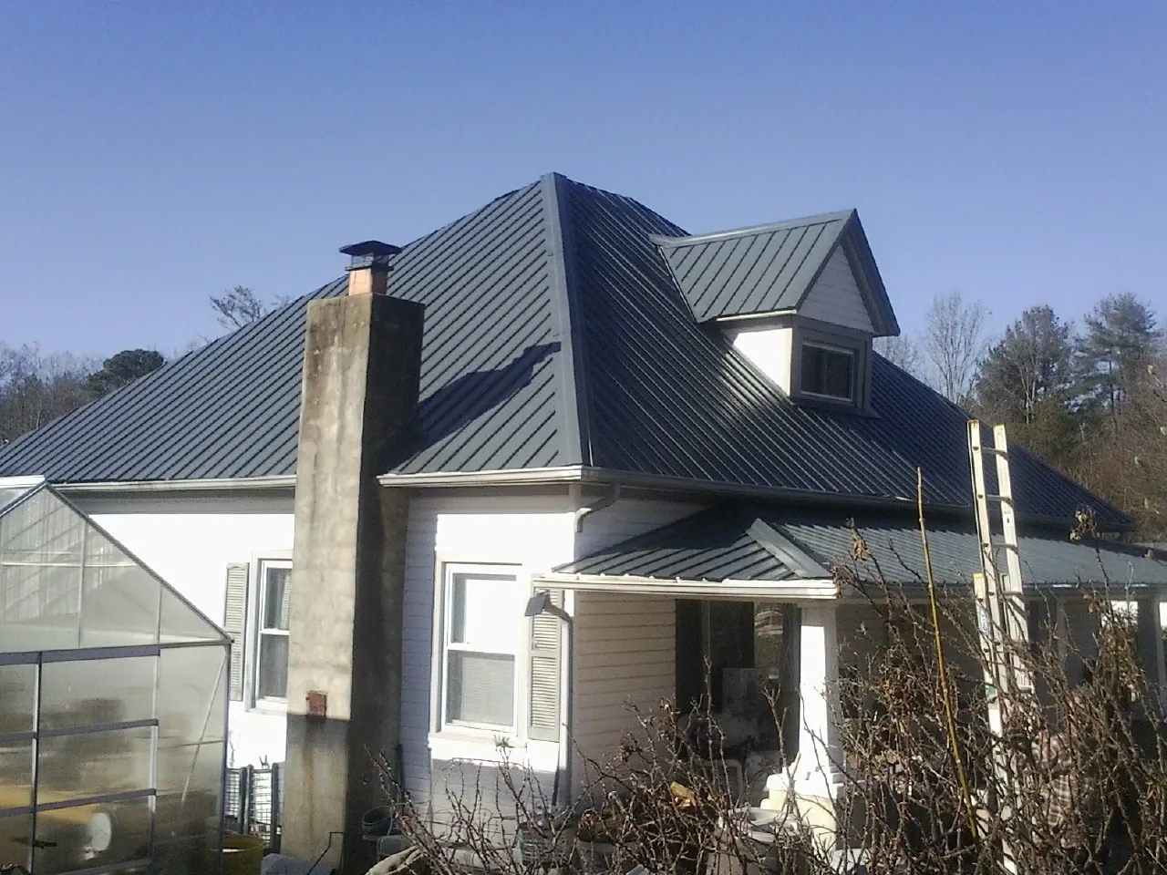 Dark blue standing seam metal roof on a white farmhouse with dormer — Slate & Tile Roof Repair by Roofing Brothers in Middlebury