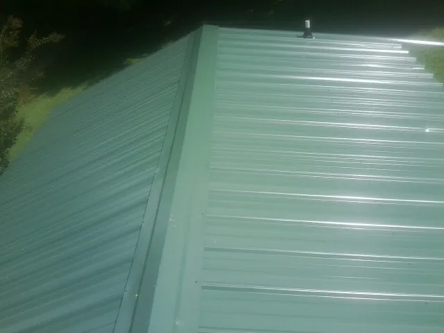 New green metal panels meeting at the ridge of a roof — Flat Roof Repair work by our crew in Middlebury