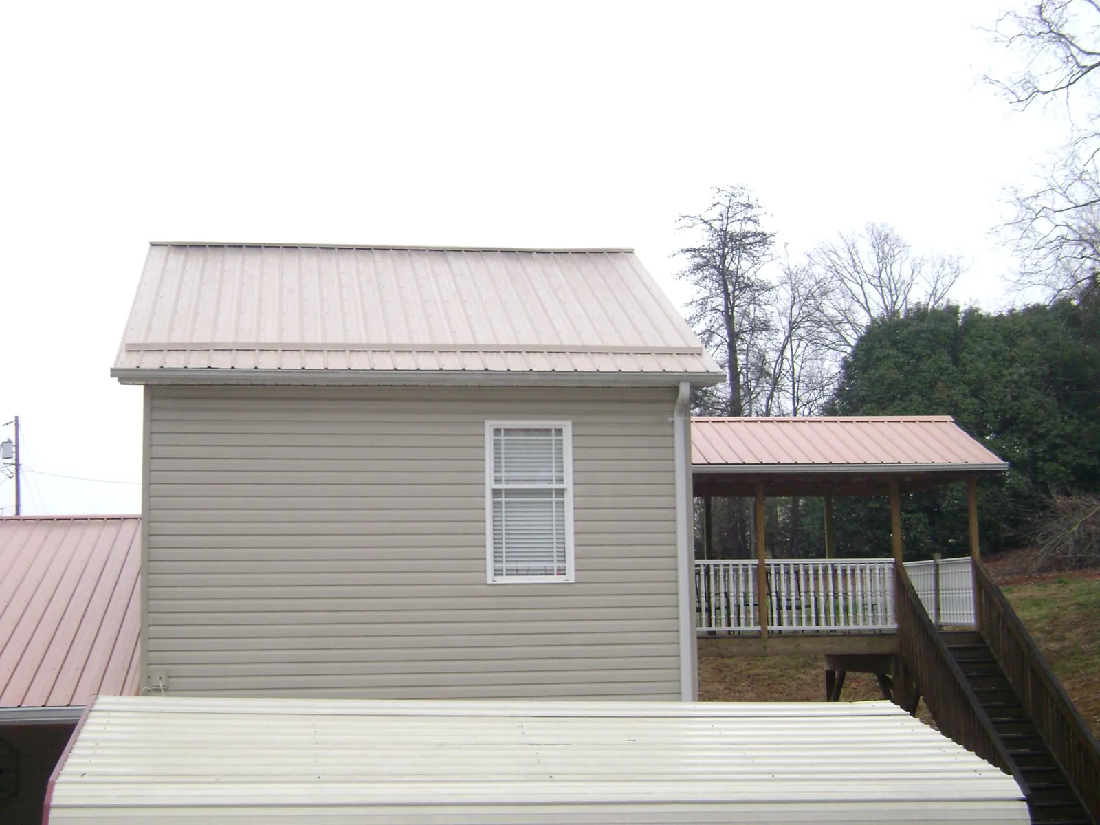 Tan metal roofs on a two story addition and attached porch, from a Roof Replacement job in Middlebury